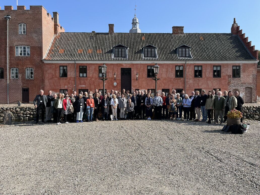 Gruppebillede af større forsamling på omkring 50 personer foran sidefløj til herregården Broholms hovedbygning.